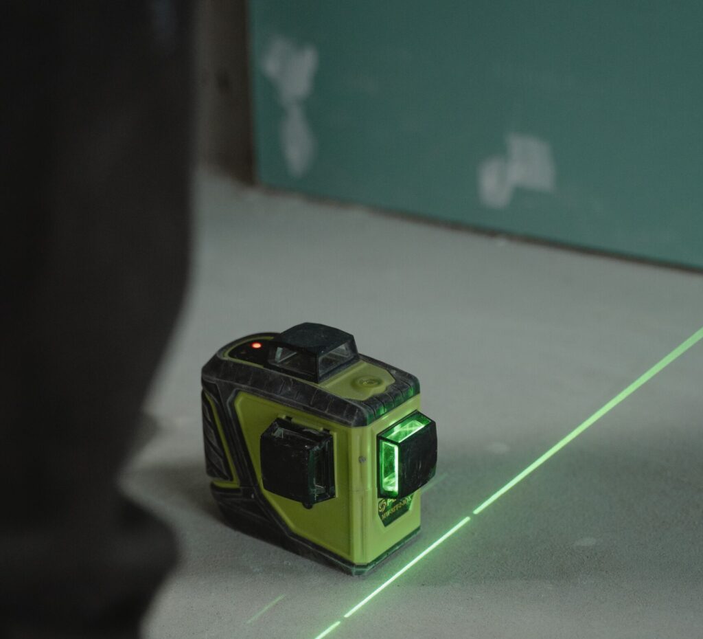 Zbliżenie zielonego lasera poziomującego używanego do precyzyjnych pomiarów na podłodze placu budowy.